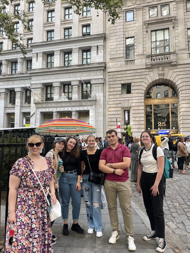 Group of students from different cultures and countries standing with their advisor on Wall Street