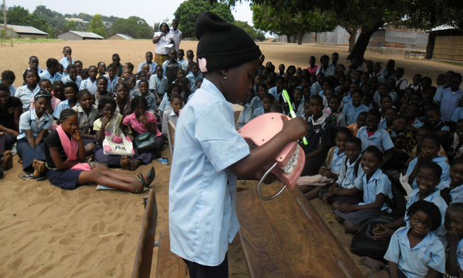 Small child in Africa showing other children how to brush teeth with a giant toothbrush and large set of fake teeth.