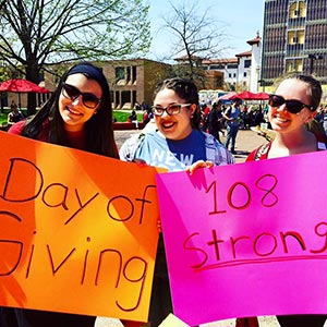 Three female Montclair State University students holding posters on Day of Giving.