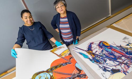 Photo of gallery curators holding Warhol prints.