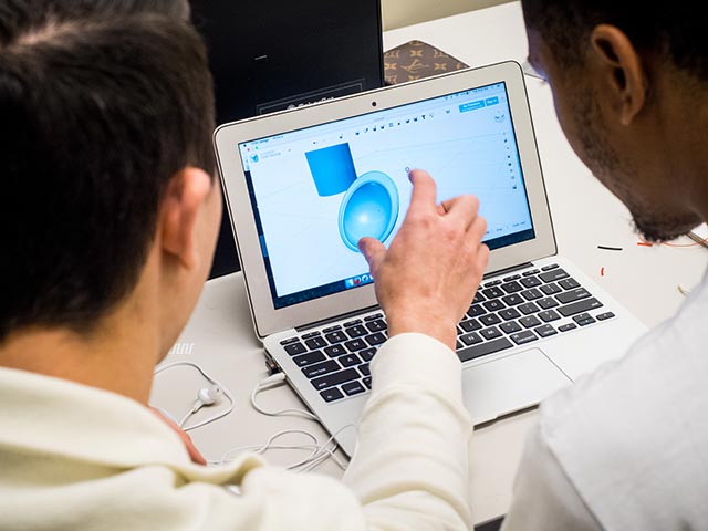 Photo of two students doing computer modeling on a laptop.