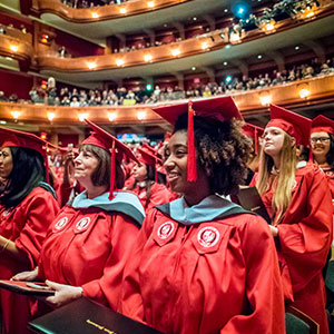 Female student clad in gown sitting in Commencement.