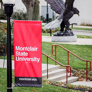 Montclair State University's banner on lightpole, with Red Hawk Statue in background.