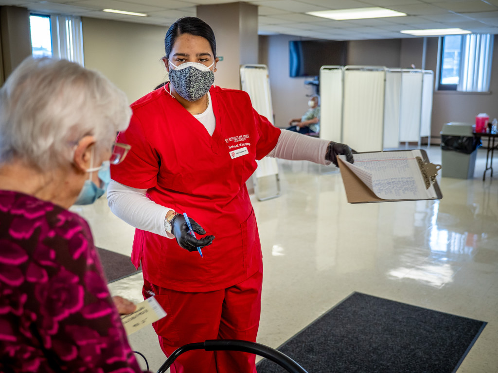 Aisha Shabbir, a sophomore BSN student, directs a resident to her inoculation. “I was just taking names and they thanked me over and over,” says Shabbir. “We started talking and I told them about my life and they told me about theirs.”