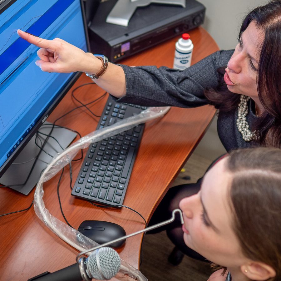 Professor and student in speech lab inspecting an audio waveform on a computer monitor