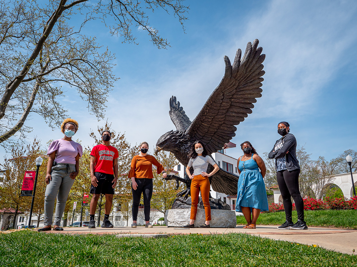 Six students in masks standing outside in front of Montclair State's hawk statue