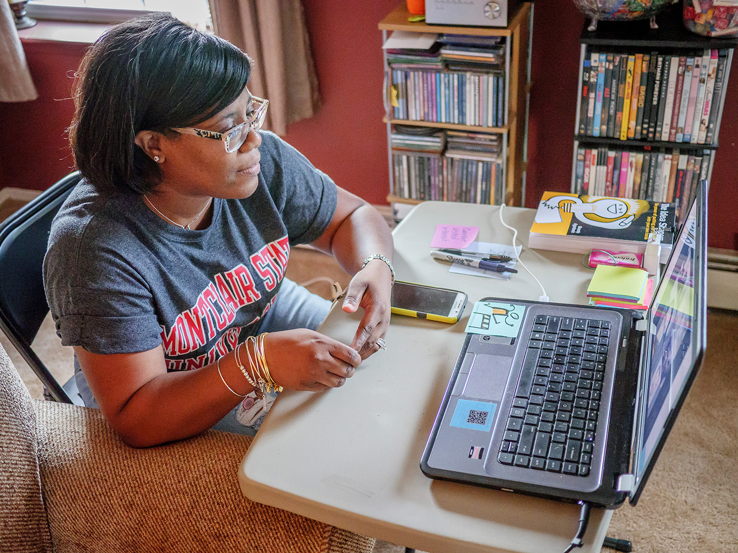 student wearing Montclair State University t-shirt sitting with laptop