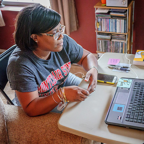 student wearing Montclair State University t-shirt sitting with laptop