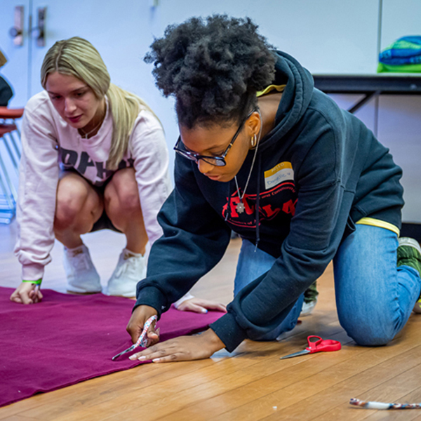 Student kneeling on floor to cut fabric