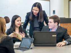 Photo of faculty and students pointing at something on an iPad.