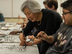 Professor in Calligraphy class drawing spiral on newspaper in front of student at the College of Humanities and Social Sciences