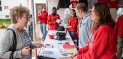Girl wearing red Montclair State University sweatshirt helping an elderly woman at Homecoming tent.