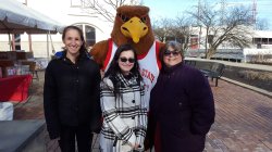 Three people standing with Rocky the Red Hawk