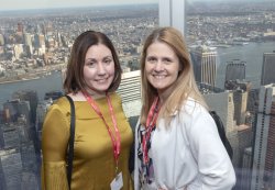 Two alumni standing in front of window overlooking city skyline