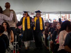 Alumni wear caps and gowns walking at Commencement