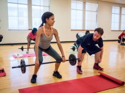 A female lifting a barbell and a man next to her instructing her.