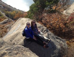 Two girls sitting on a rock at an overlook on a sunny day