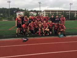 Large group of men looking at the camera and huddled together. On a sports field wearing red and black