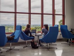 Two students sitting in the School of Communication and Media on their laptop discussing something.