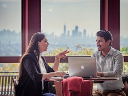 Graduate students talk to one another with New York City skyline in the distance.