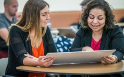 two women sitting at table looking at poster