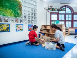 Photo of teacher with two young students playing blocks.