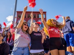 Students excited cheering at a football game on a sunny day