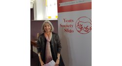 professor Lucy McDiarmid standing in front of event banner