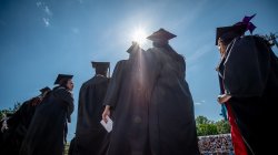 photo of students in black cal and gown with sunlight behind them
