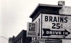 black and white image of old building with large advertisement painted on side. Sign reads Brains 25 cents
