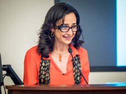 Photo of Professor Teresa Fiore in orange blazer standing and speaking at a podium