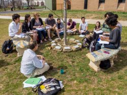 a creative writing class sitting outside for class. students and instructor are seated on benches and in the grass