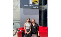 Drs. Nina Kaiser and Daniela Peterka-Benton stand for a photo together outside. A sign for Universit Graz is behind and above them