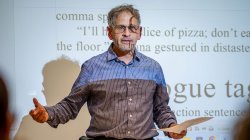 "David Galef, with his lesson projected onto his face and the screen behind him, talks to students."