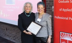 two people stand smiling, one is holding a certificate
