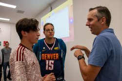 A college professor speaking to two student speaking to two students after class. Everyone is standing and dressed casually.