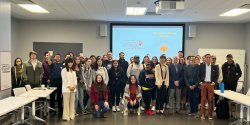 A group of more than 20 faculty and students standing together smiling in front of a large projection screen at a 2022 event that highlighted social media pumpkin spice findings.