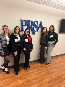 A group of five students standing and smiling with the letters P R S S A on the wall behind them.