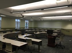 Another example of a breakout room/lecture hall. Some chairs with rounded tabletops surround a single lectern.
