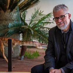 Dr. Scott Kight sitting by the dinosaur exhibit in the CELS Atrium