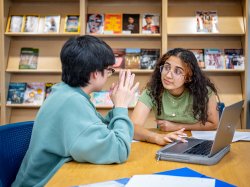 Students talking in library with laptop in front of them