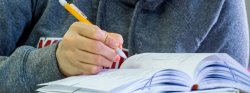 Close up of a book and a student writing.