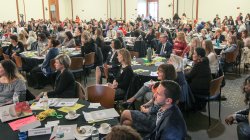 People seated at tables in crowded conference room.