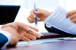 close up of hands holding pens and paper as two people discuss paperwork at a desk.