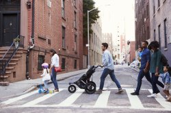 Man pushing stroller and other people crossing a street.