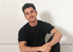 Headshot photograph of a seated man wearing a black shirt, black pants.