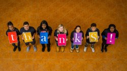 Students looking up at the camera and holding up signs that spell out, thanks!