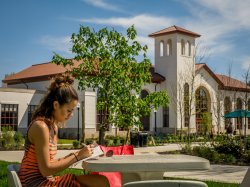 Photo of student highlighting content in book while sitting at an outside table on campus on a sunny day.