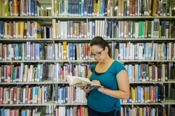 Student reading book in library in front of shelves