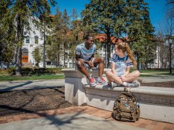 Two students laughing outside with each other on a sunny day outside of a college building.